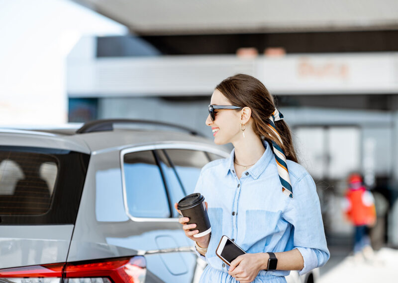 Young woman having a coffee break standing near the car on the gas station