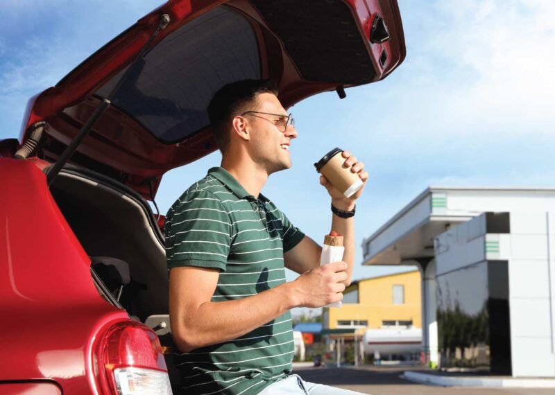 Man Eating & Drinking Next to Car