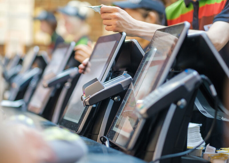 Row of order kiosks with computer screens and card payment terminals in fast food restaurant