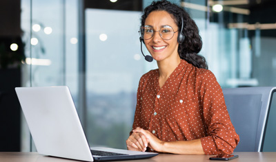 Smiling female customer support representative wearing headset and sitting at desk with laptop