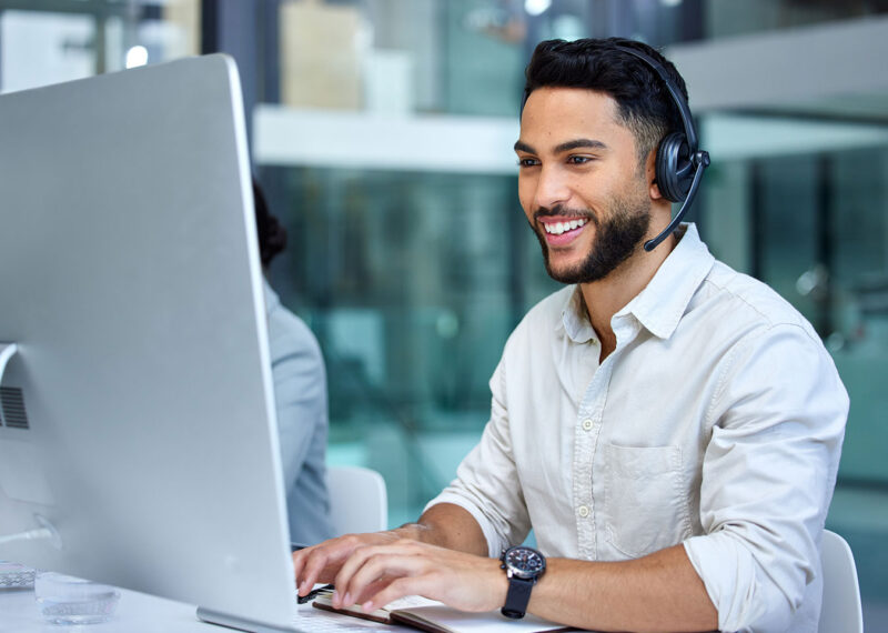 Business man, call center and web support communication at a computer in a office. Phone conversation, smile and male worker with contact us, crm and customer service job