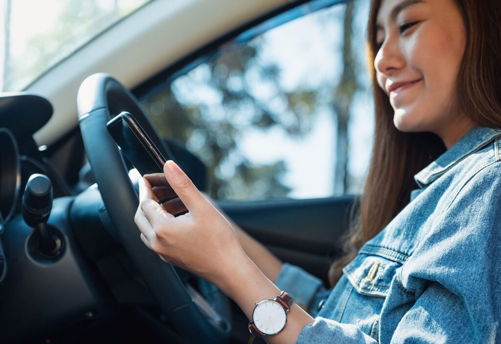 Woman using consumer application while sitting in driver's seat of car.