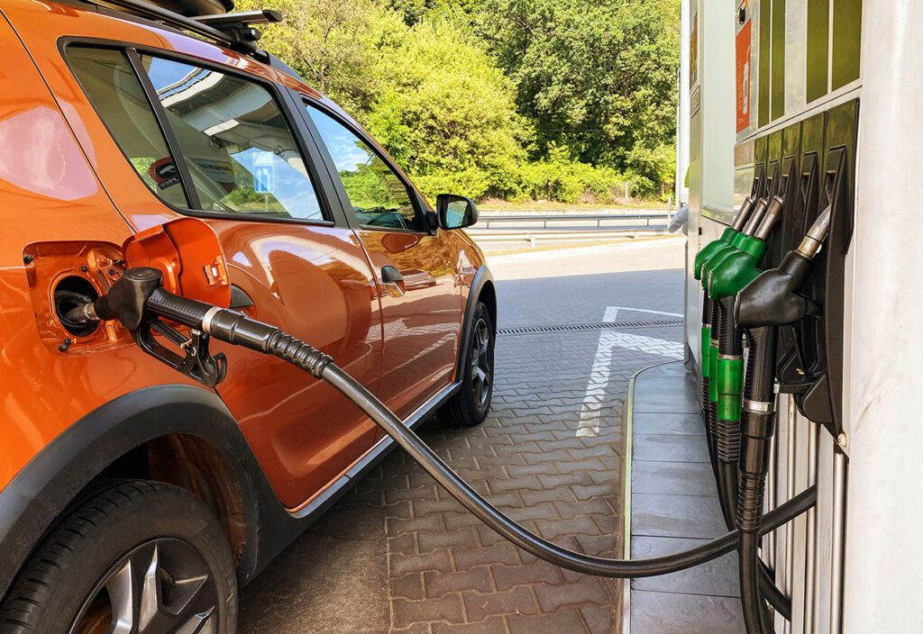 Orange car parked in front of fuel pumps at gas station with pump inserted into tank.
