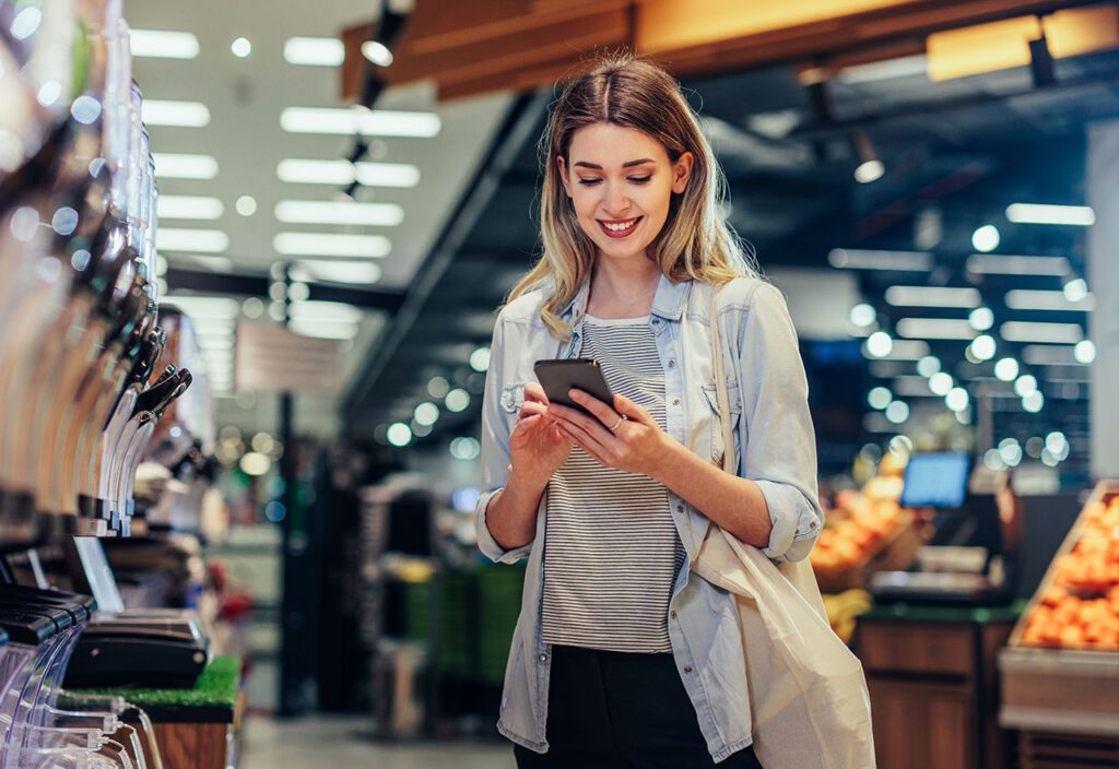 Woman in grocery store standing in front of bulk bins looking at shopping list on phone.