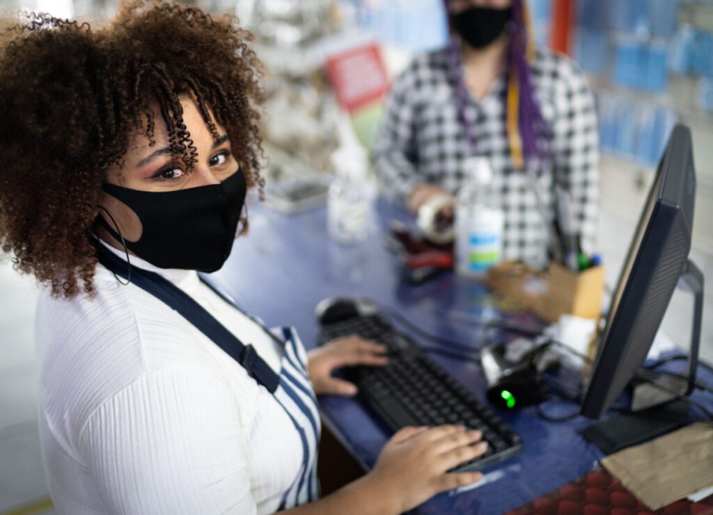 Convenience retail industry female cashier wearing a mask using POS to ring up a customer.