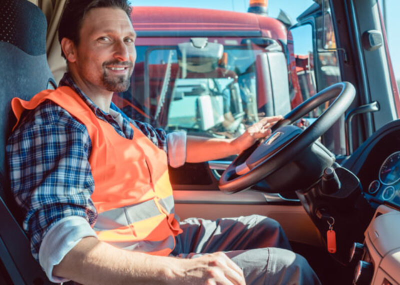 man sitting in a truck at the wheel wearing orange vest