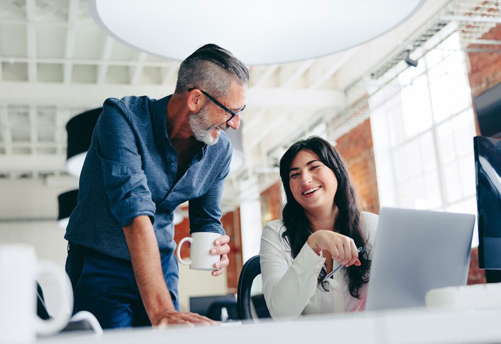Two coworkers chatting and working in front of computer at office.