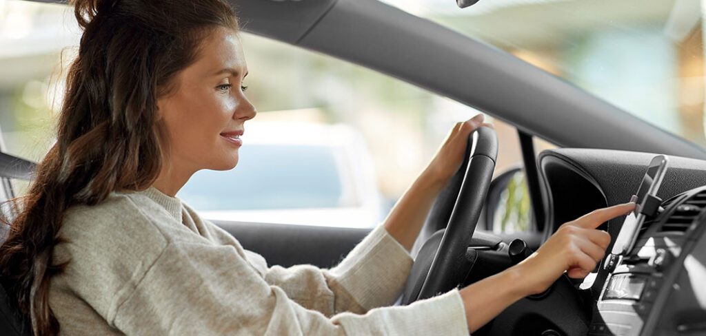 Woman in driver's seat of car using cell phone to find fuel rewards on GasBuddy.