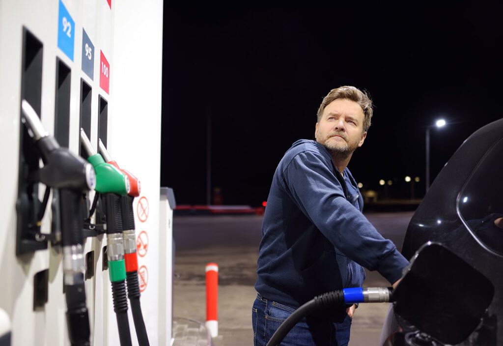 Man fueling up car at convenience retail location with fuel pumps in foreground.