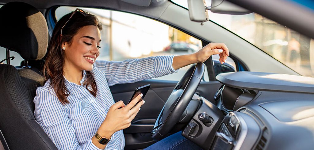 Business woman sitting in car and using her smartphone.