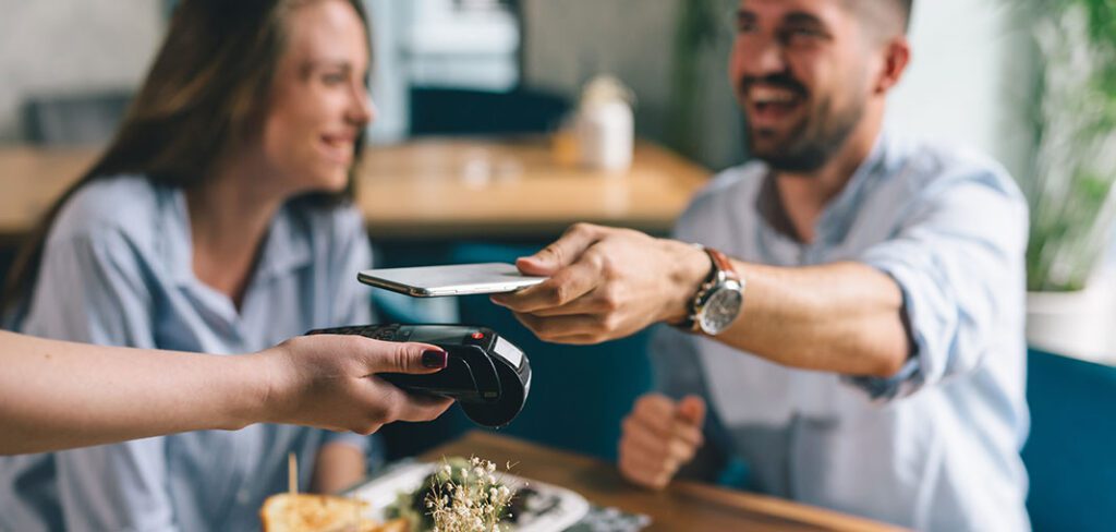 Man in restaurant using phone to make contactless payment at wireless merchant terminal.
