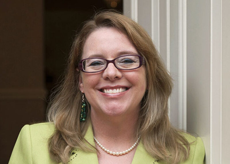 woman smiling wearing glasses and green blazer