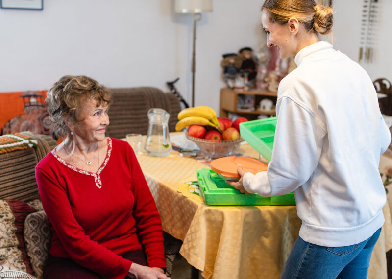 Young woman delivering meal to older woman in her home