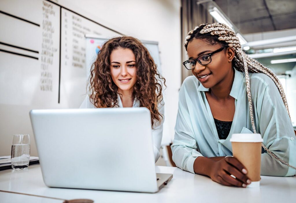 Two women colaborating at the computer over coffee