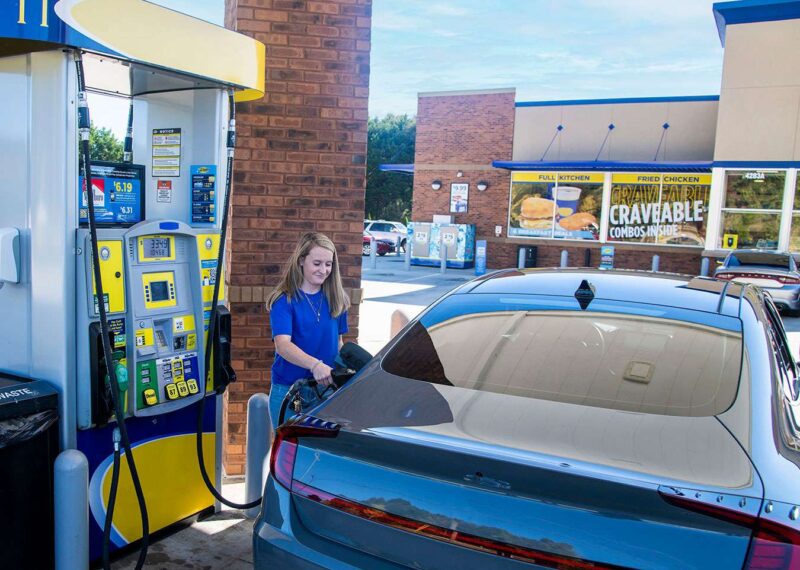 Young woman filling up her car gasoline tank at a convenience store