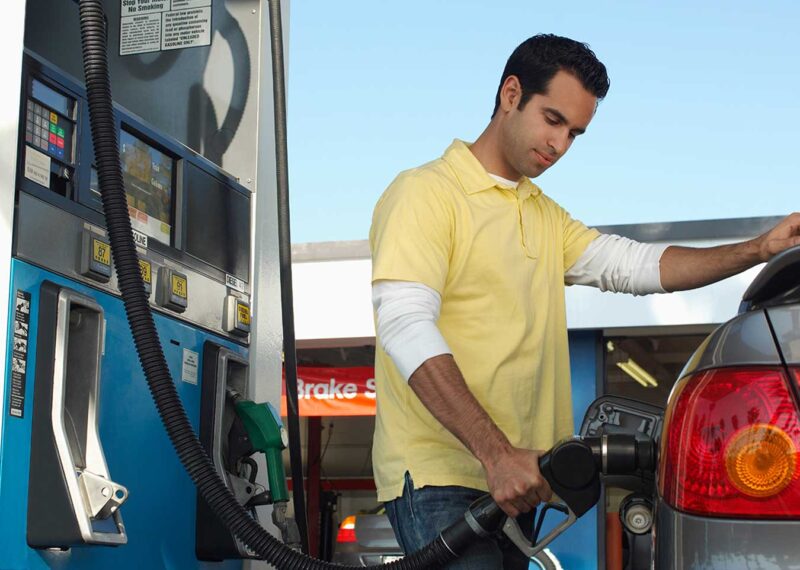 Young man pumping gas into car at gas station