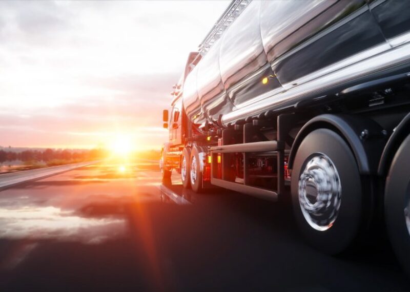 A fuel truck driving towards a sunset