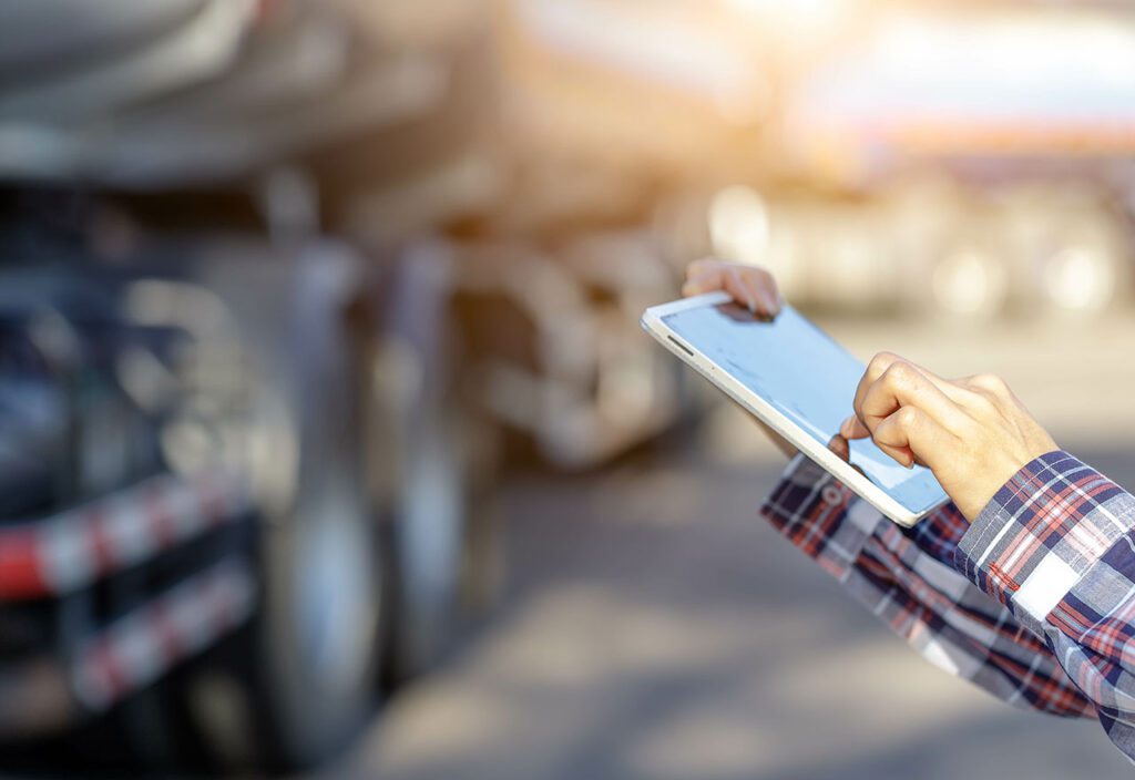 Truck driver's hand holding tablet to manage truck and delivery fleet.