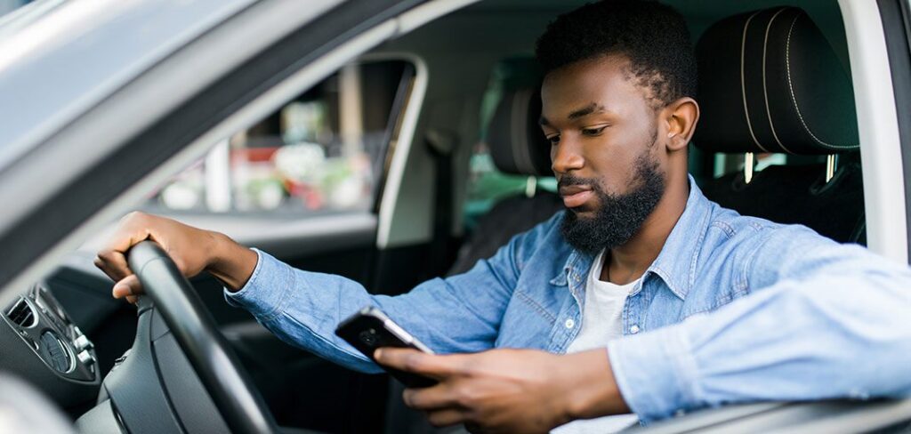 Young male African American holding his phone while driving his car.