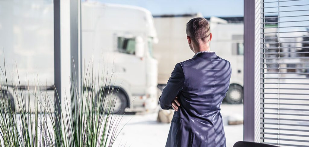 Trucking logistics manager looks out of the window at fleet of parked trucks.