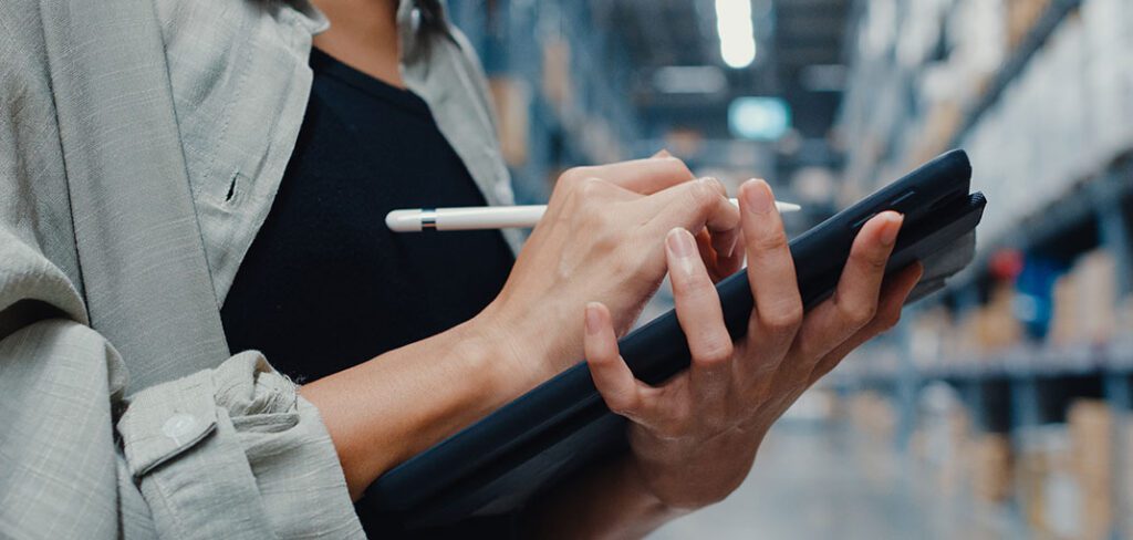 Manager using tablet to check inventory levels in back-office of warehouse.