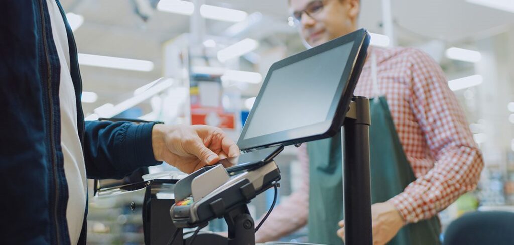 Customer at CPG store using cell phone to make touchless payment at merchant terminal.