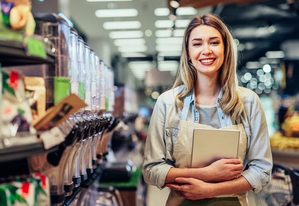 Female CPG store employee smiling in aisle of grocery store products.