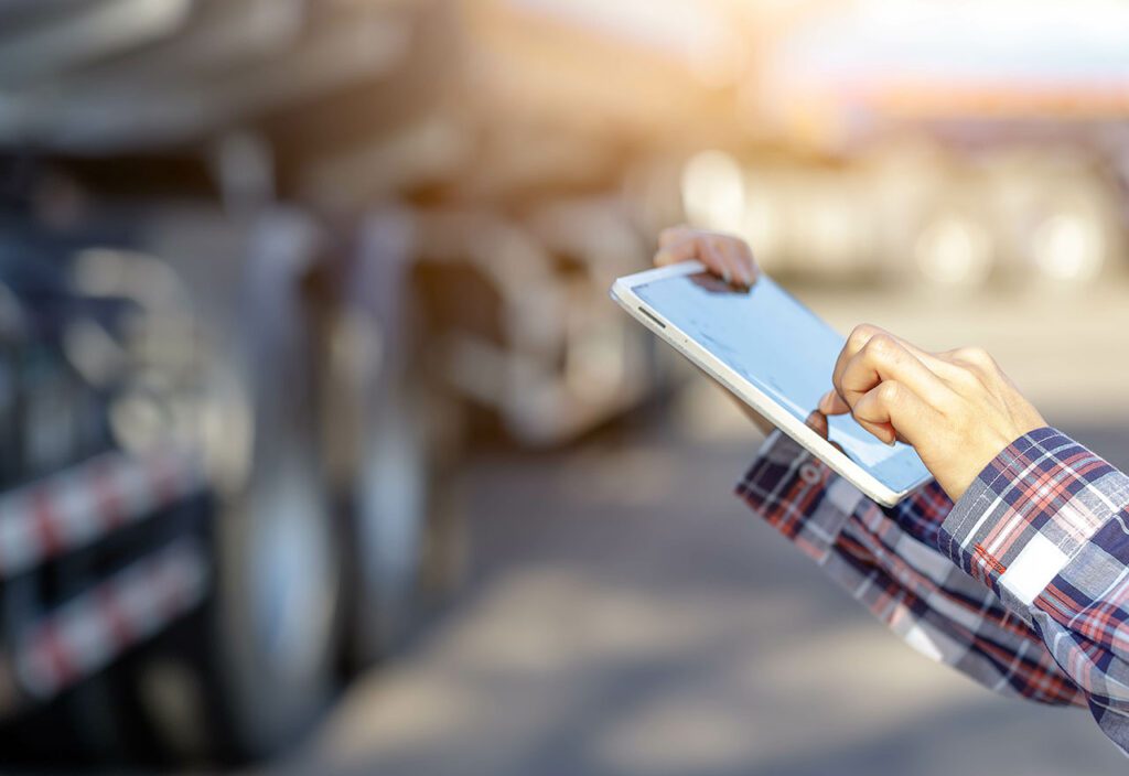 Logistics manager using tablet with fuel truck in background.