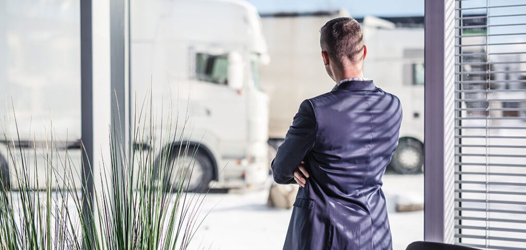 Trucking company manager looks out of the window and fleet of parked trucks