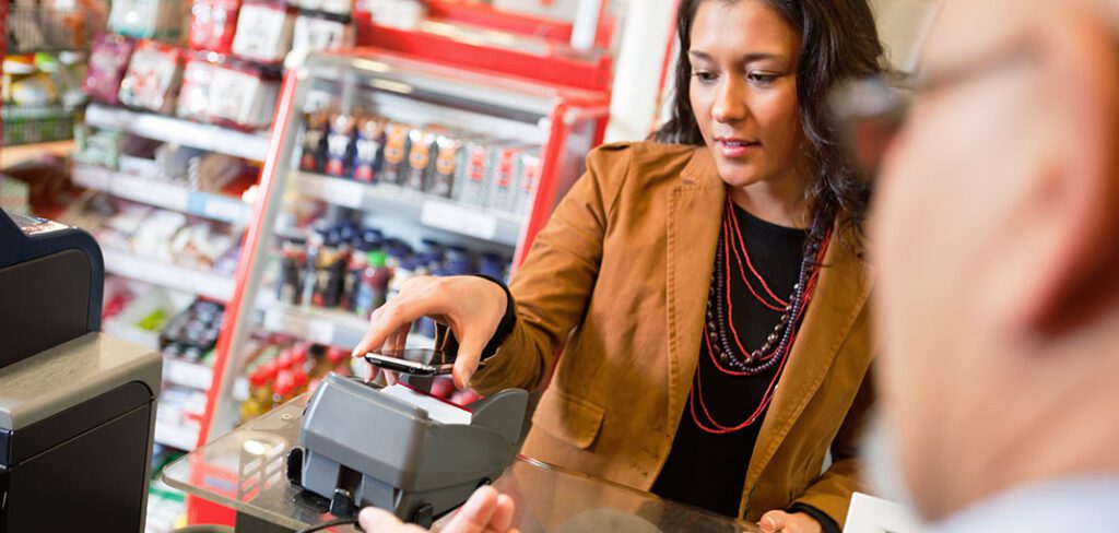 Woman using smart mobile phone to pay at merchant terminal in convenience store.