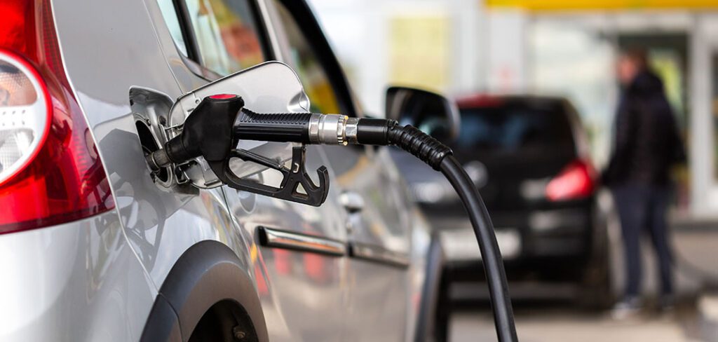 Close up of silver car with fuel pump inserted into fuel tank at gas station.