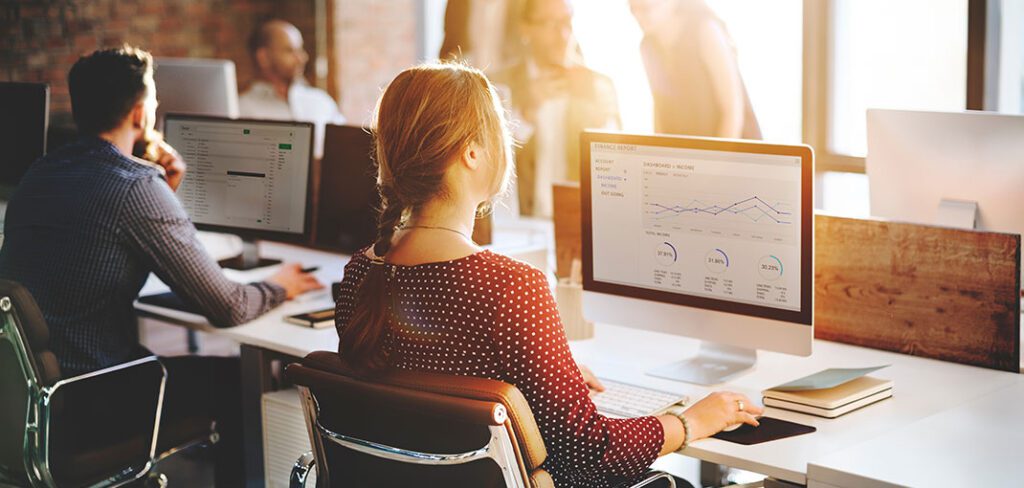 Open office with multiple computers and employees viewing finance success graphs.