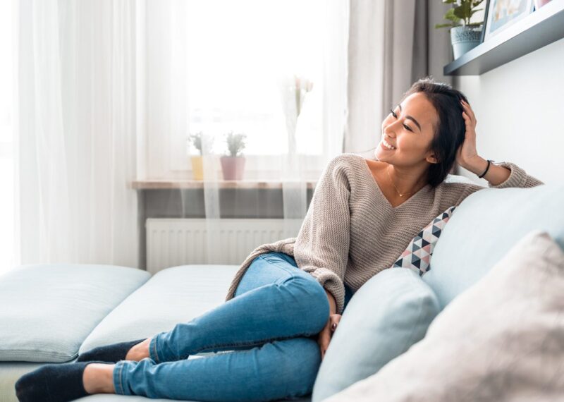 Relaxed smiling Asian woman sitting on sofa warm at home.