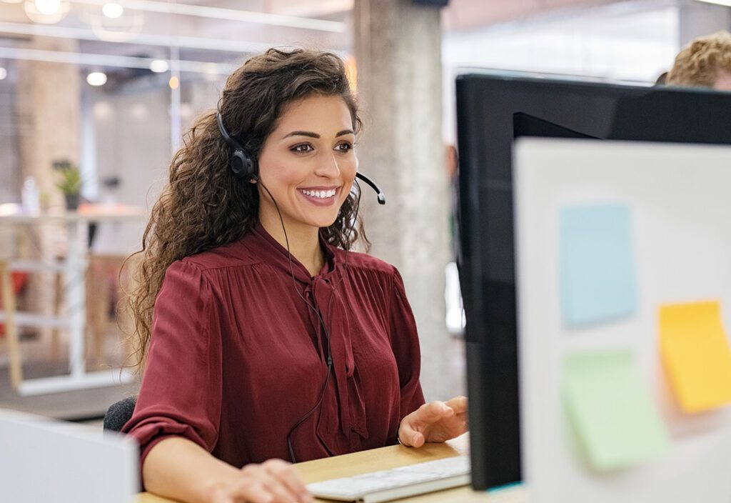 Female call center employee wearing headset providing customer support on computer.