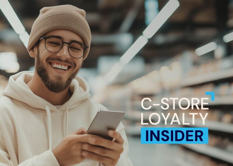 Smiling customer on a mobile device in a convenience store using a smartphone, representing loyalty engagement in C-store marketing.