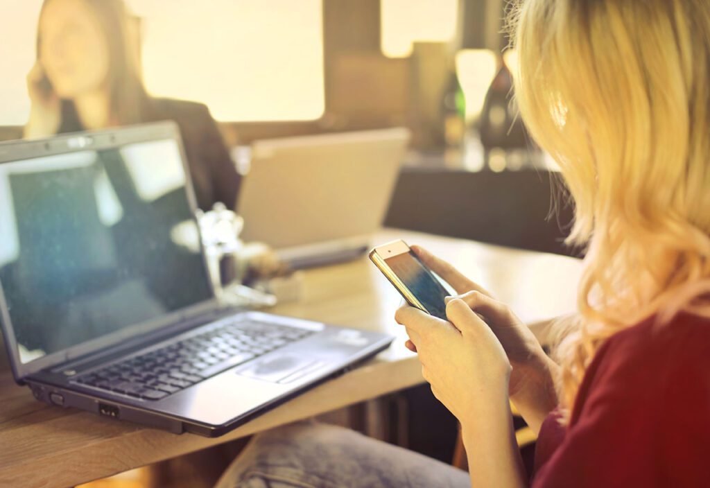 Woman sitting in front of open laptop using cell phone in back office.