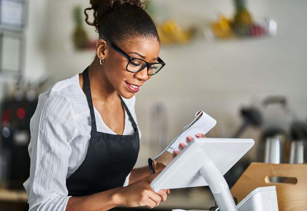 Employee entering order using pos point of sale terminal at register in restaurant.