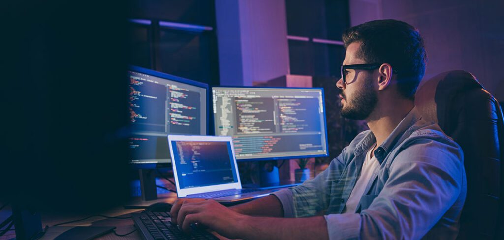 IT data specialist at desk working in front of three computer screens.
