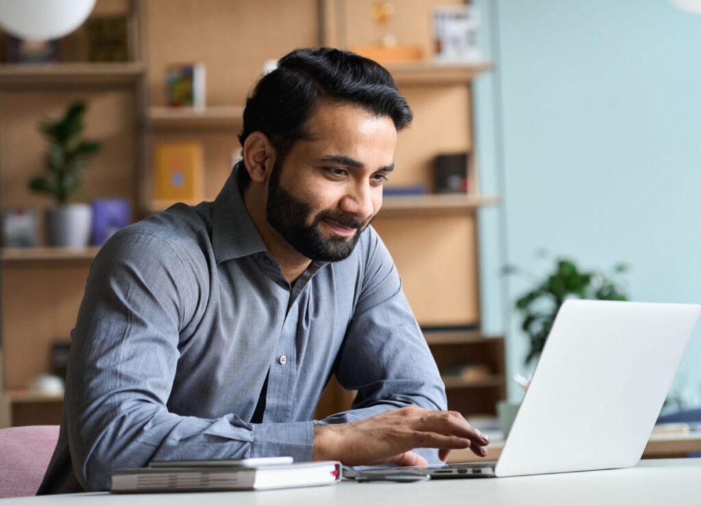 man sitting at table smiling and looking at laptop