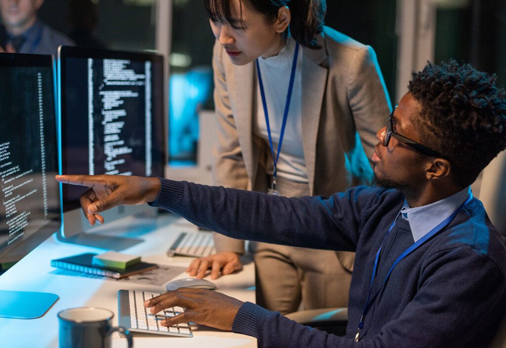 Two young colleagues discussing coded data on computer screen while businessman points at it.