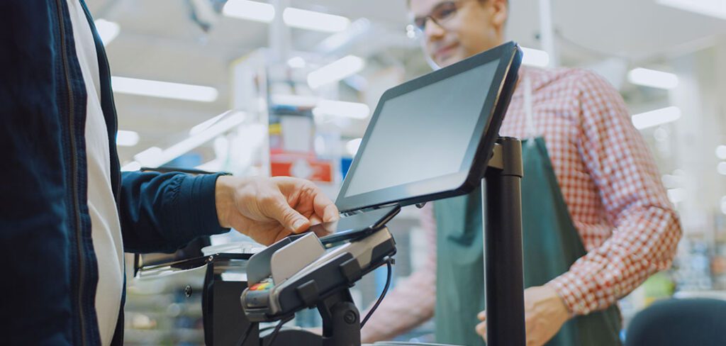 Cashier at CPG retail store holding cell phone against merchant terminal to accept wireless payment.