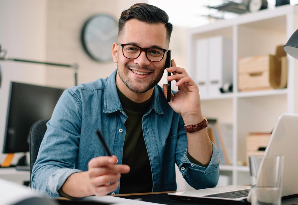 A Man is smiling while taking on his mobile phone at the workplace