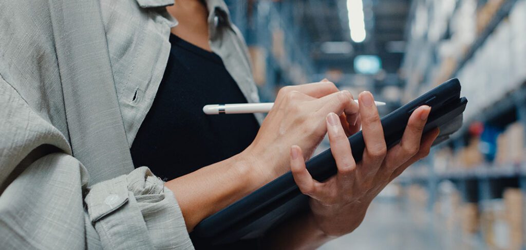 Manager using tablet to check inventory levels in back-office of warehouse.