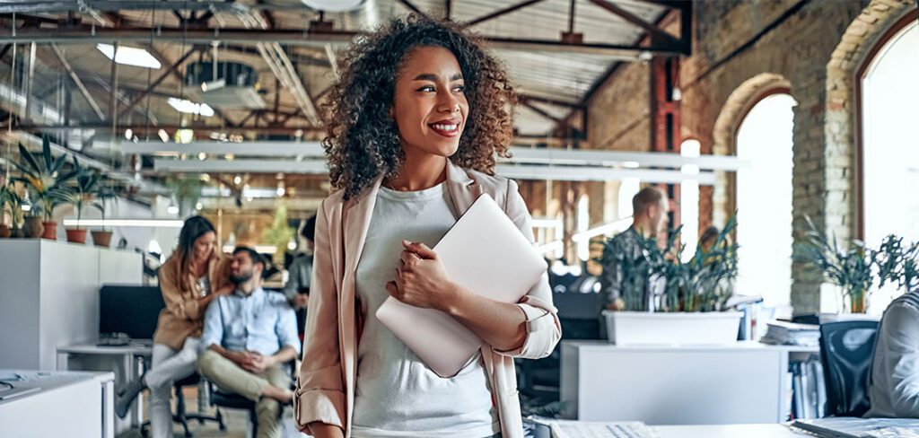 Woman in office holding a laptop walking through her office.