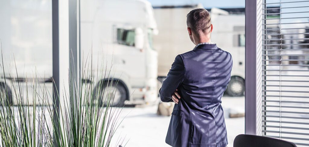 Man standing in front of window looking out on fleet of trucks.