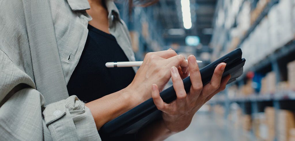 Manager using tablet to check inventory levels in back-office of warehouse.