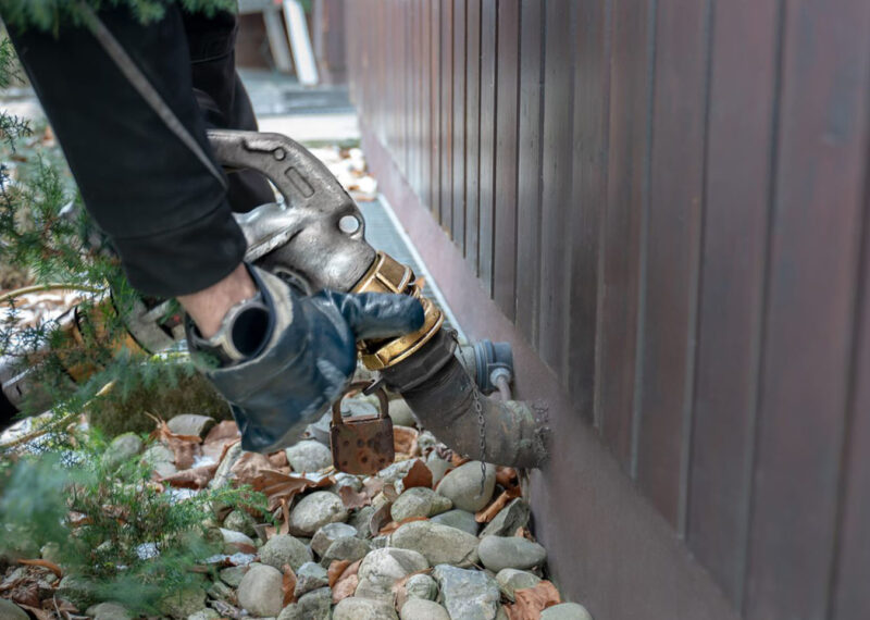Man wearing gloves and attaching a hose for fuel oil delivery. The hose carries the oil to the tank in the house for heating.